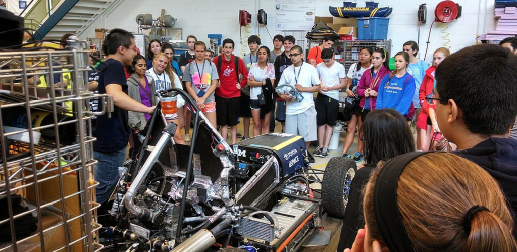 A group of people gathered around a person presenting a car